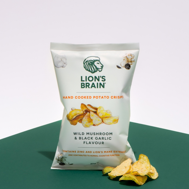 A bag of Lion's Brain Hand Cooked Potato Crisps in Wild Mushroom & Black Garlic Flavour, displayed on a dark green surface against a white background with a few crisps scattered in front.