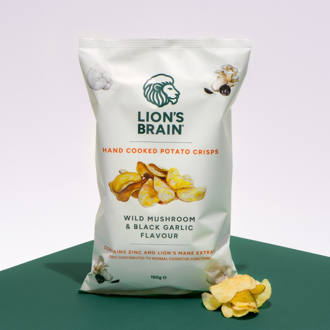 An orange bag of Lion's Brain hand cooked potato crisps, labelled 'Wild Mushroom & Black Garlic Flavour', standing on a dark green surface against a light grey background with a few crisps scattered in front.