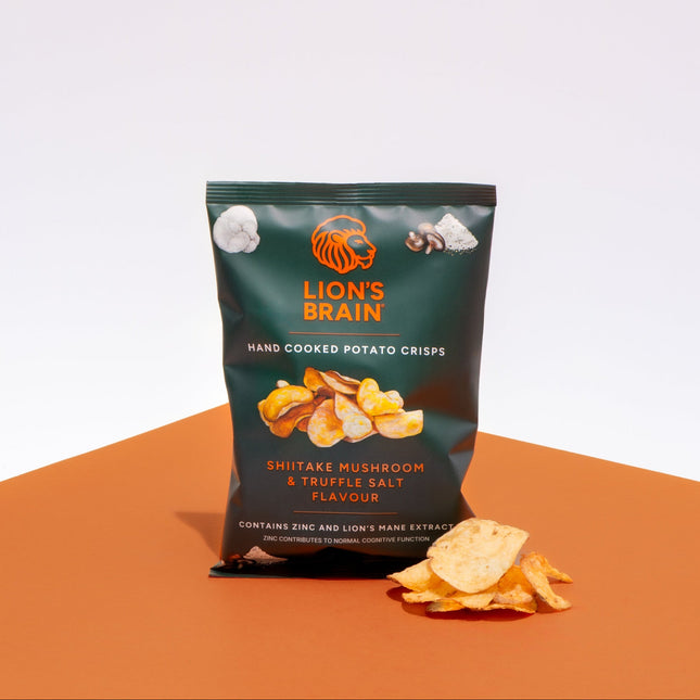 A bag of Lion's Brain hand cooked potato crisps in Shiitake Mushroom & Truffle Salt flavour, displayed on an orange surface against a white background with a few loose crisps in front.