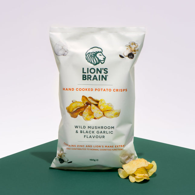 A 150g bag of Lion's Brain Hand Cooked Potato Crisps in Wild Mushroom & Black Garlic Flavour, displayed on a dark green surface against a light grey background with a few crips scattered in front.