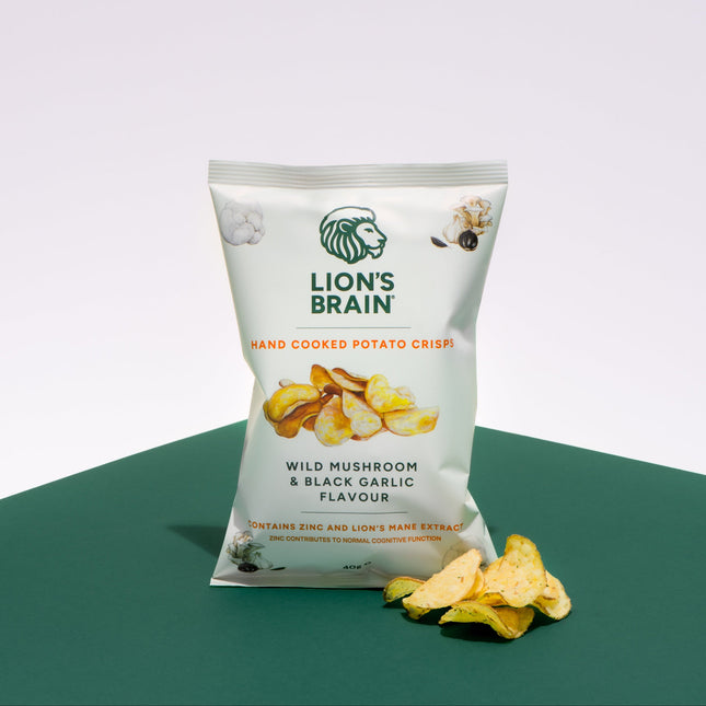 A bag of Lion's Brain Hand Cooked Potato Crisps in Wild Mushroom & Black Garlic Flavour, displayed on a dark green surface against a white background with a few crisps scattered in front.